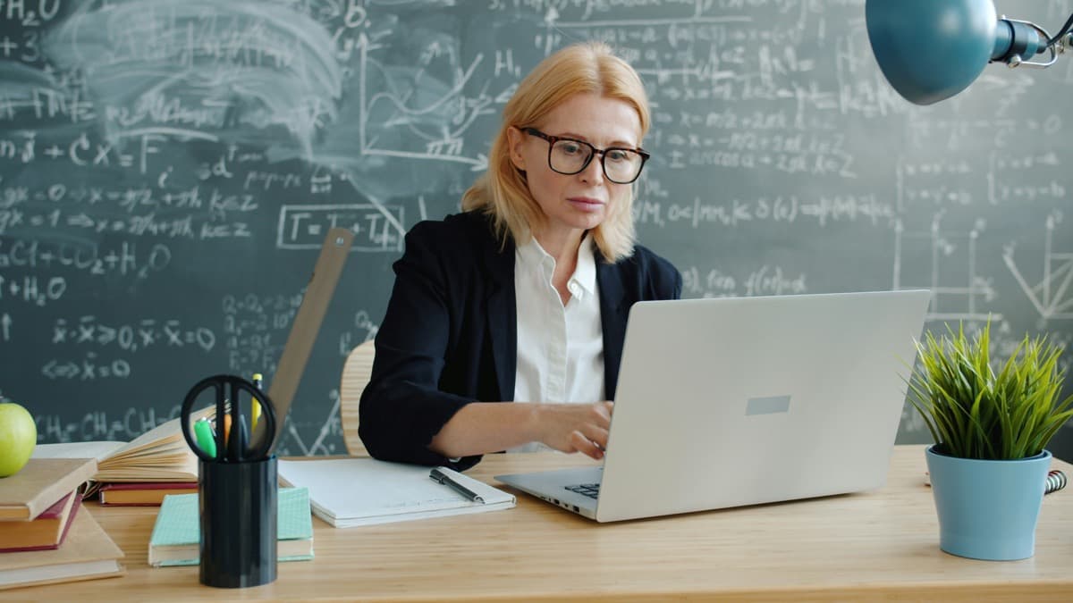 Professeure effectuant sa déclaration SAP en ligne sur son ordinateur portable, devant un tableau de formules mathématiques